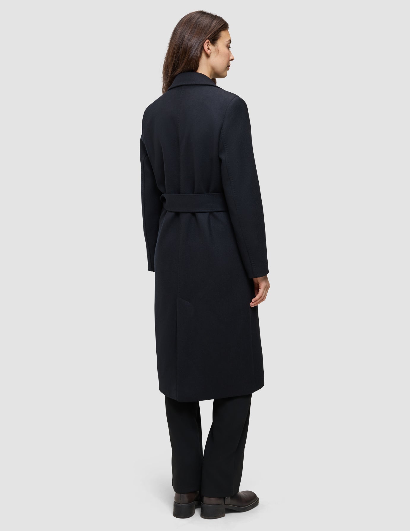 A woman viewed from the back wearing a Women’s Wool Coat Black, featuring a long Scandinavian design with a belted waist.